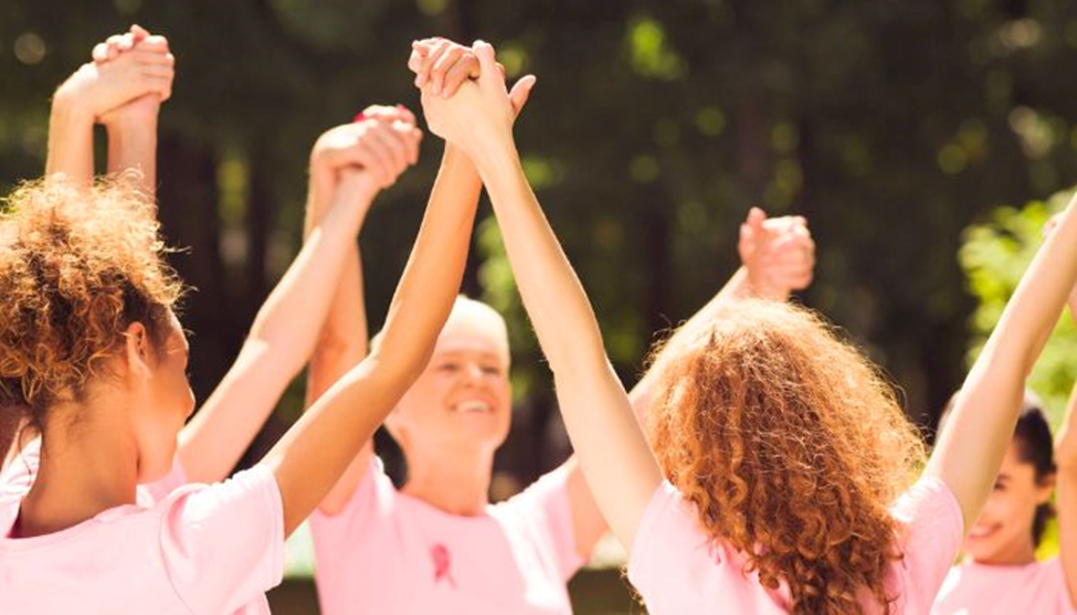 woman in a group holing hands in the air with pink shirts 